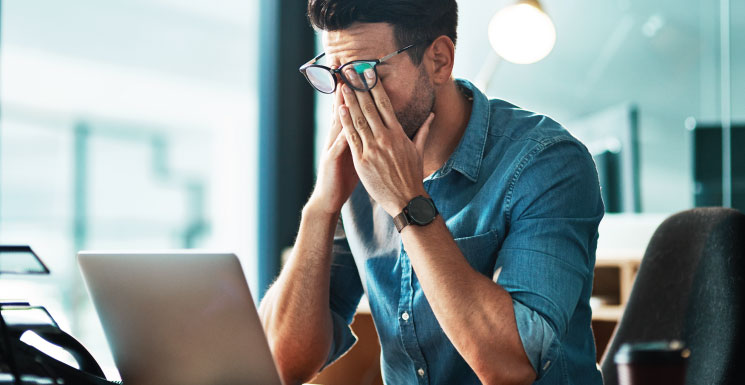 Worried man at laptop with hands on his face, overwhelmed by a financial issue.