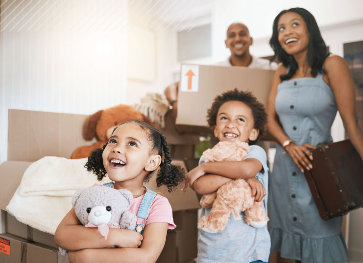 Family unpacking boxes with kids holding stuffed animals indoors