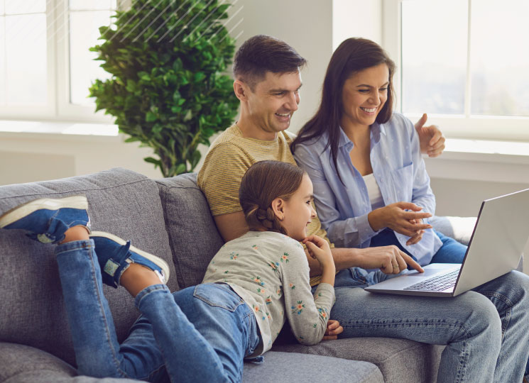 Family smiling on the couch while looking at a laptop together.