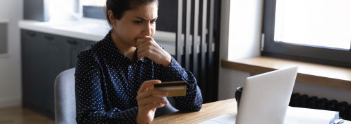 Concerned woman holding a credit card while looking at her laptop screen.