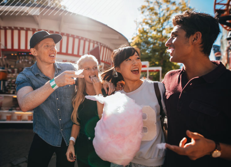 Friends laugh together while sharing cotton candy at an amusement park.