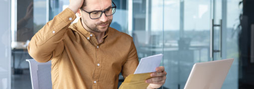 Man looking at a letter with concern while sitting at a laptop in an office.