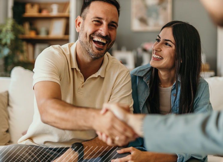 Couple smiles while shaking hands with another person during a meeting at home.