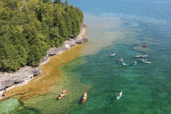 Kayakers exploring the clear shoreline of Door County, Wisconsin near a wooded bluff.
