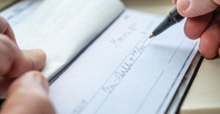Close-up of someone writing a check with a pen.