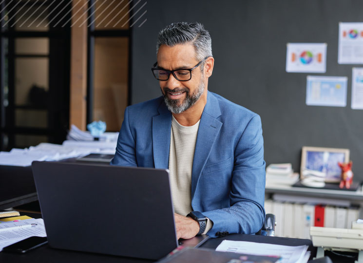 Businessman smiling while working on laptop in a modern office setting.