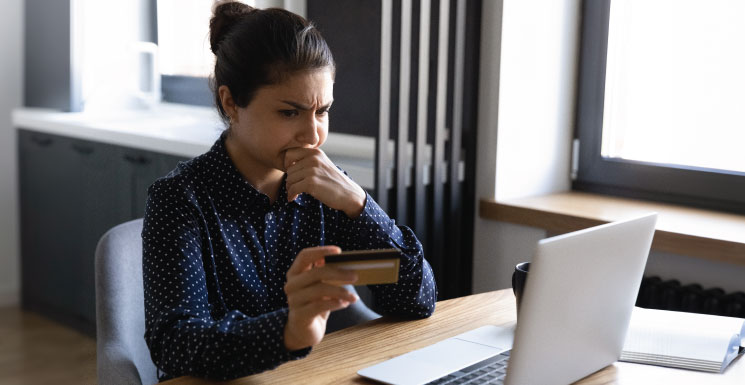 Concerned woman holding a credit card while looking at her laptop screen.