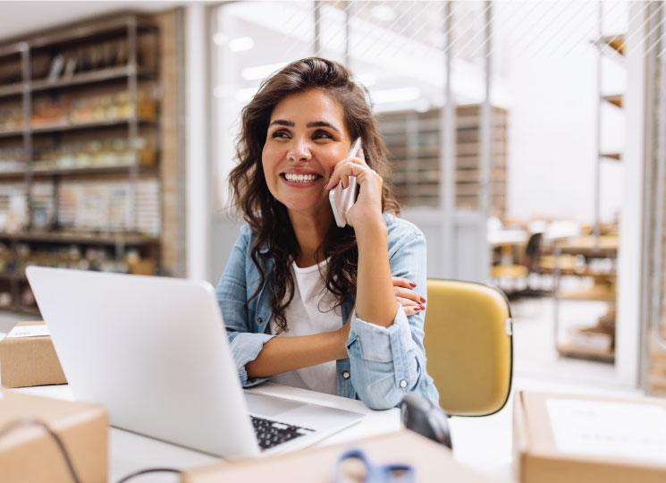 Small business owner smiling while talking on the phone at her desk with a laptop