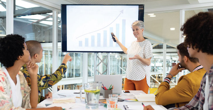 Businesswoman leading a small business workshop, presenting a growth chart to a group at a conference table.