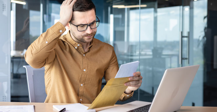 Man looking at a letter with concern while sitting at a laptop in an office.